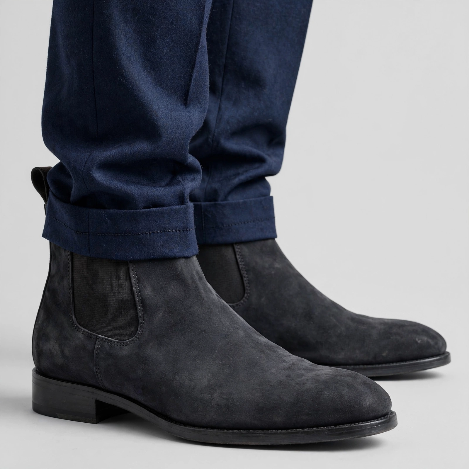 close-up shot from the shins down of a man wearing cuffed navy blue suit trousers and dark charcoal grey suede Chelsea boots.